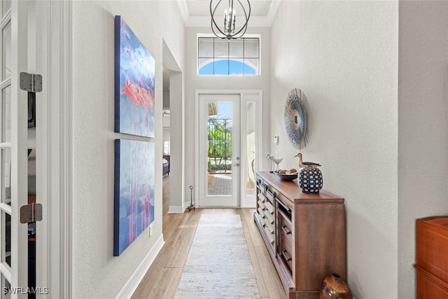 doorway with a textured wall, light wood-style flooring, ornamental molding, a chandelier, and baseboards