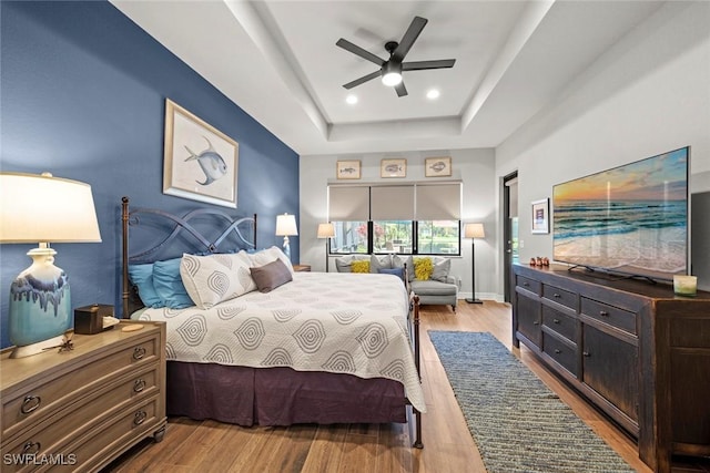 bedroom featuring baseboards, a raised ceiling, a ceiling fan, light wood-style flooring, and recessed lighting