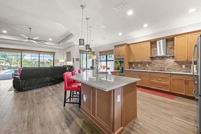 kitchen with wood finished floors, open floor plan, wall chimney range hood, and backsplash