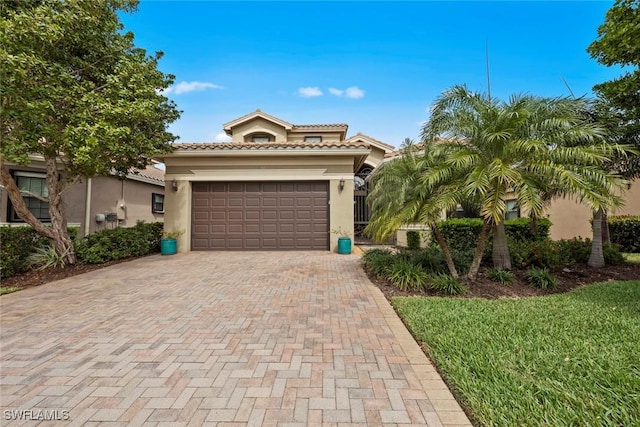 mediterranean / spanish-style house with an attached garage, a tile roof, decorative driveway, and stucco siding