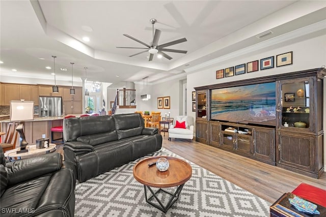 living area with light wood-style flooring, recessed lighting, a ceiling fan, stairs, and a raised ceiling