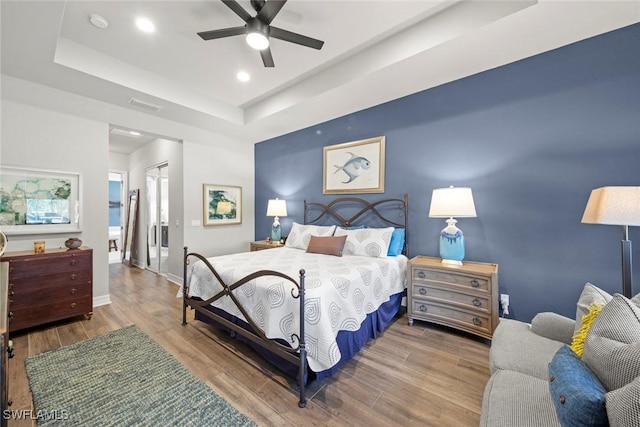 bedroom featuring a tray ceiling, wood finished floors, visible vents, and baseboards