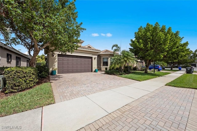 view of front of property featuring a tiled roof, an attached garage, decorative driveway, a front lawn, and stucco siding