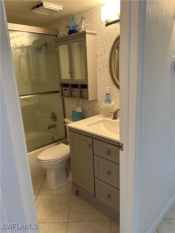 bathroom with vanity, wallpapered walls, bath / shower combo with glass door, tile patterned flooring, and toilet