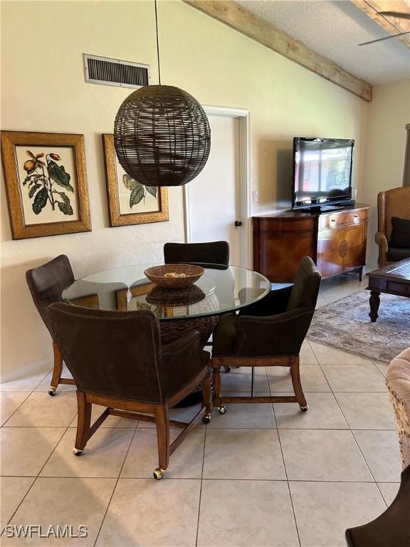 dining room with light tile patterned floors, visible vents, a textured ceiling, and vaulted ceiling with beams