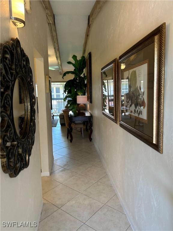 hallway with beam ceiling, a textured wall, baseboards, and light tile patterned flooring