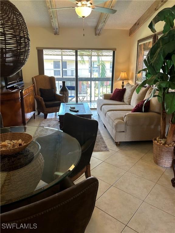 living area featuring light tile patterned floors, beamed ceiling, and ceiling fan