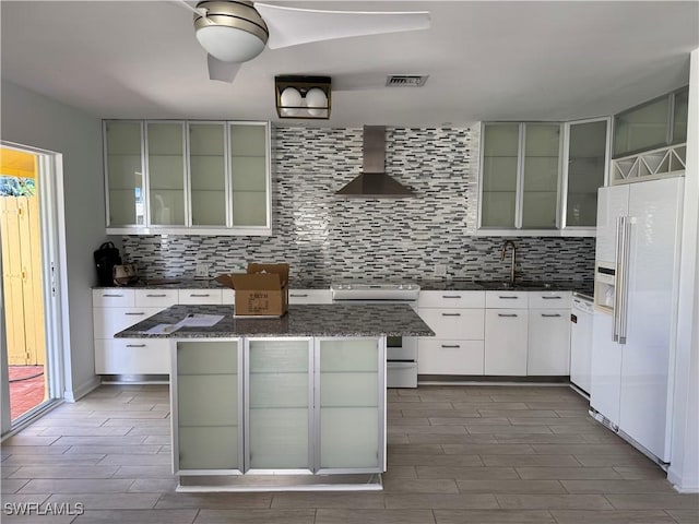 kitchen featuring wood finish floors, visible vents, backsplash, white appliances, and wall chimney exhaust hood