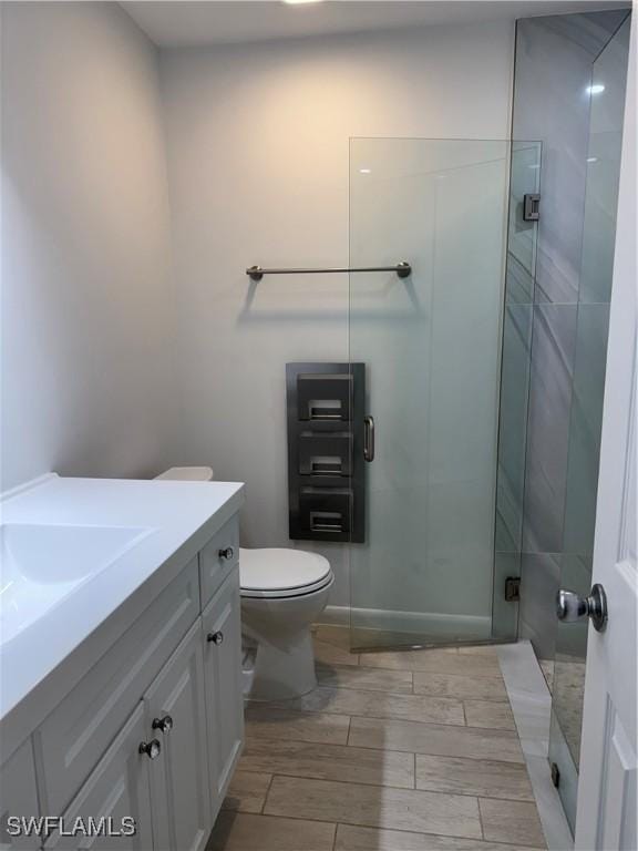 full bathroom with toilet, a stall shower, wood finish floors, and vanity