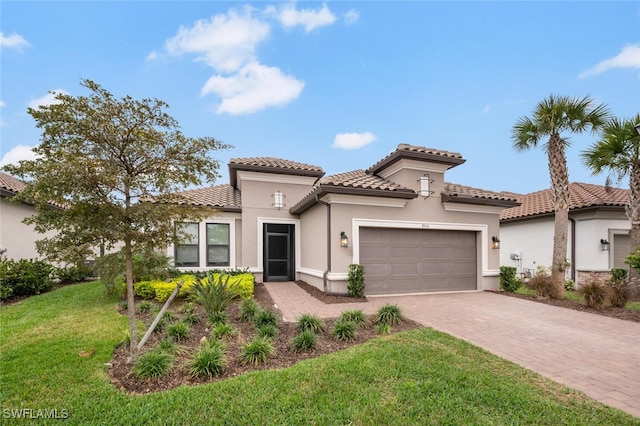 mediterranean / spanish house featuring stucco siding, a tiled roof, an attached garage, decorative driveway, and a front yard