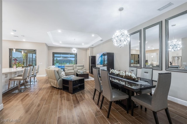 dining room featuring a tray ceiling, wood finish floors, visible vents, and an inviting chandelier