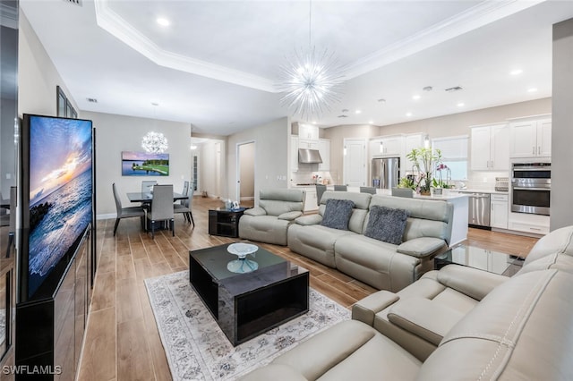 living area featuring light wood finished floors, baseboards, a raised ceiling, an inviting chandelier, and crown molding