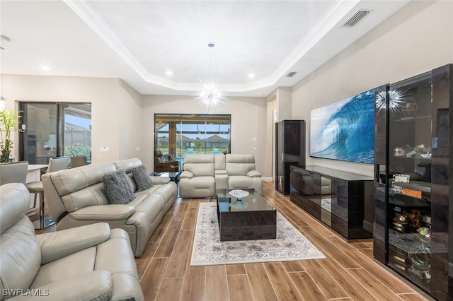 living area with wood tiled floor, visible vents, a tray ceiling, and ornamental molding