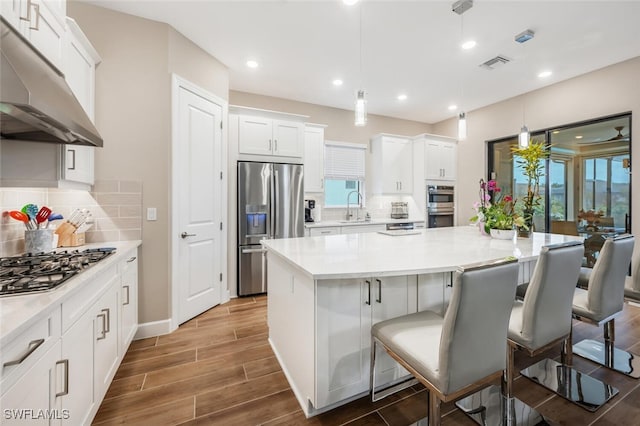 kitchen with stainless steel appliances, visible vents, wood tiled floor, a sink, and under cabinet range hood