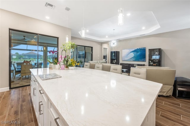 kitchen with light stone counters, a raised ceiling, white cabinets, and wood tiled floor