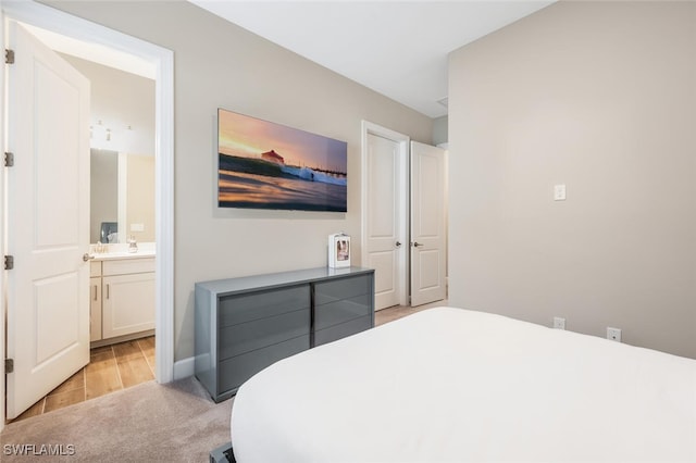 bedroom with light carpet, light wood-style flooring, and ensuite bathroom