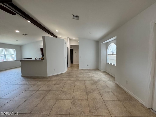 empty room featuring vaulted ceiling with beams, plenty of natural light, visible vents, and light tile patterned flooring