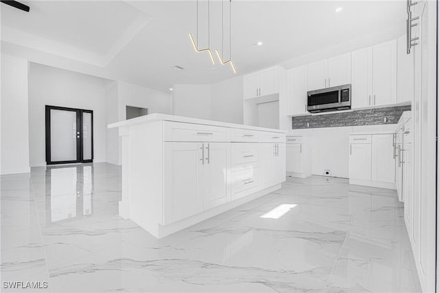 kitchen featuring marble finish floor, white cabinetry, stainless steel microwave, and decorative light fixtures