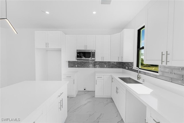 kitchen with a sink, white cabinetry, marble finish floor, tasteful backsplash, and stainless steel microwave