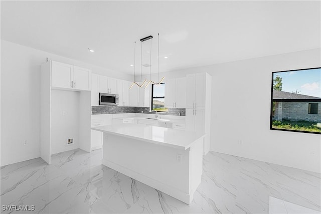 kitchen featuring a kitchen island, stainless steel microwave, hanging light fixtures, white cabinetry, and a sink