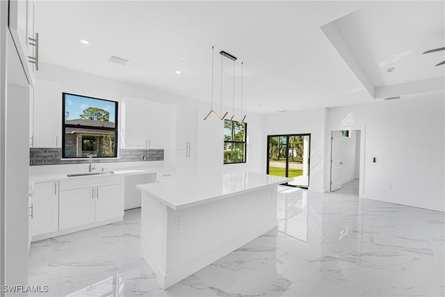 kitchen with a kitchen island, a sink, visible vents, white cabinets, and marble finish floor