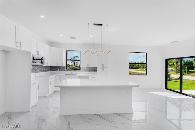 kitchen featuring stainless steel microwave, plenty of natural light, white cabinetry, and decorative backsplash