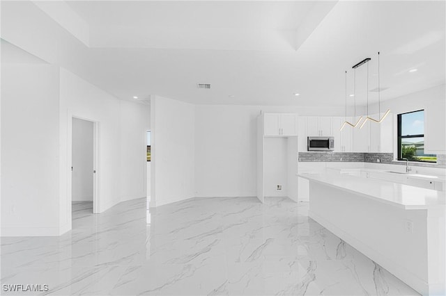 kitchen with white cabinets, stainless steel microwave, marble finish floor, light countertops, and a sink