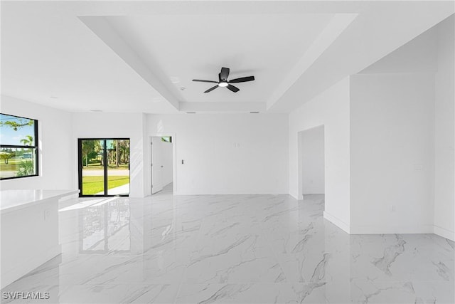 unfurnished room featuring a ceiling fan, a raised ceiling, marble finish floor, and baseboards