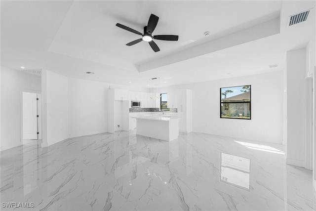 unfurnished living room with marble finish floor, a tray ceiling, visible vents, and a ceiling fan