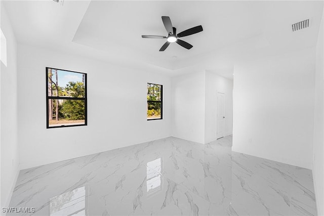 spare room with marble finish floor, visible vents, a raised ceiling, and a ceiling fan