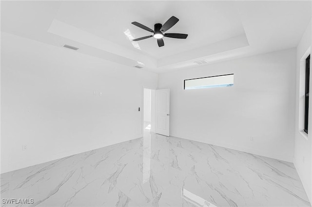 empty room featuring ceiling fan, visible vents, and a raised ceiling