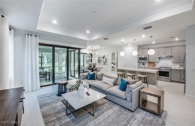 living area with ornamental molding, a raised ceiling, visible vents, and a notable chandelier