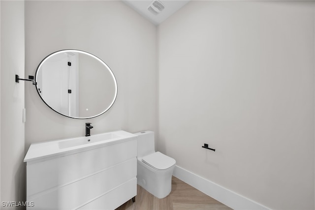 half bath featuring toilet, wood finished floors, visible vents, vanity, and baseboards