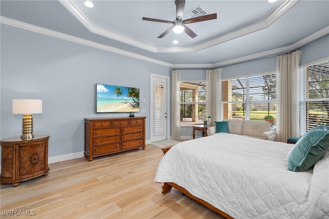 bedroom with light wood-style floors, a raised ceiling, and multiple windows