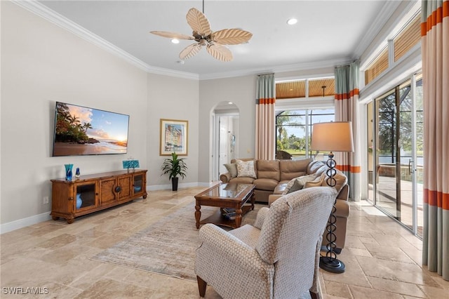 living area with arched walkways, stone tile floors, a ceiling fan, baseboards, and crown molding