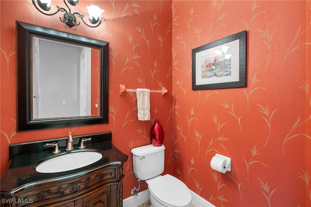 half bath with baseboards, vanity, toilet, and wallpapered walls