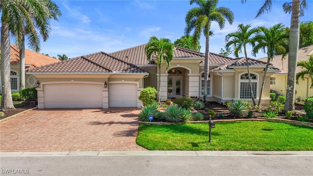 mediterranean / spanish home with decorative driveway, a tiled roof, an attached garage, and stucco siding