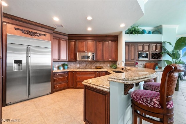 kitchen featuring a breakfast bar area, a sink, appliances with stainless steel finishes, light stone countertops, and tasteful backsplash