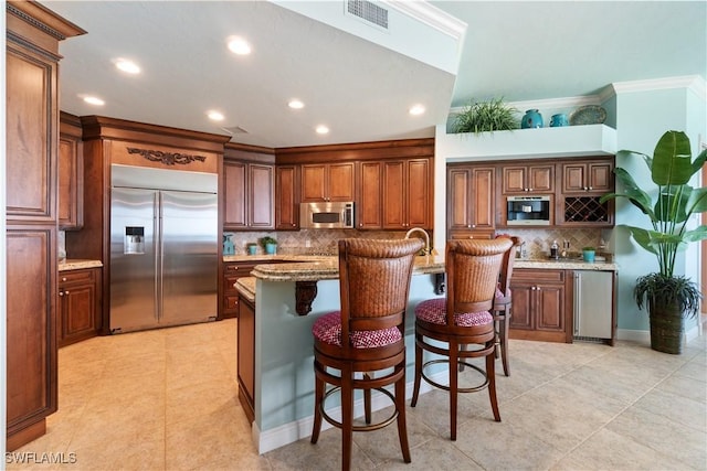 kitchen featuring stainless steel appliances, a center island with sink, visible vents, and light stone countertops