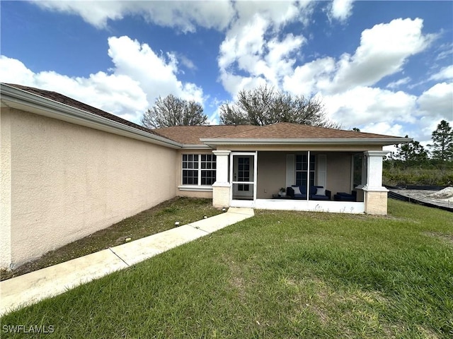 back of house featuring roof with shingles, a lawn, and stucco siding