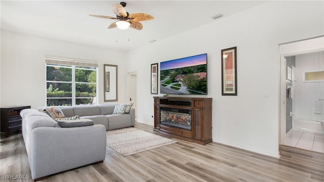 living area featuring baseboards, visible vents, a glass covered fireplace, ceiling fan, and wood finished floors