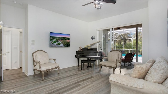 living area featuring a sunroom, a ceiling fan, baseboards, and wood finished floors