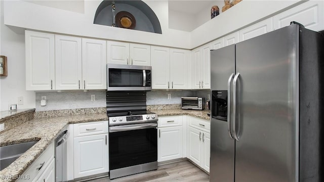 kitchen featuring appliances with stainless steel finishes, white cabinets, decorative backsplash, and light stone countertops