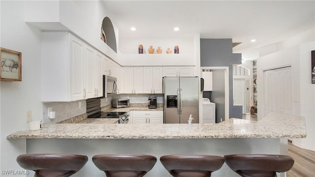 kitchen with washer / dryer, decorative backsplash, a breakfast bar, a peninsula, and stainless steel appliances