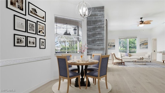 dining area featuring light wood-style flooring, baseboards, and ceiling fan with notable chandelier