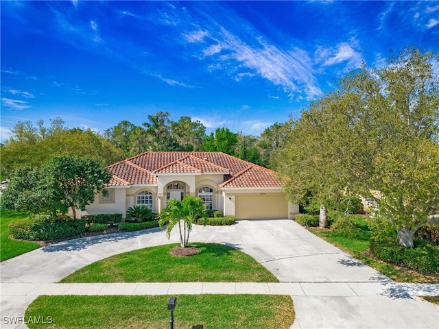 mediterranean / spanish house with a tile roof, stucco siding, a front yard, a garage, and driveway