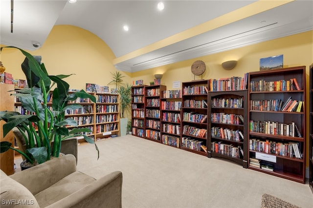 sitting room featuring vaulted ceiling, wall of books, and carpet flooring