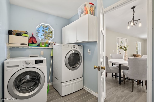 clothes washing area with baseboards, wood finish floors, washer and clothes dryer, a chandelier, and cabinet space