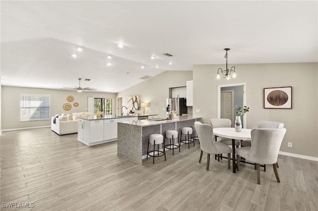 dining room featuring visible vents, lofted ceiling, ceiling fan with notable chandelier, light wood-style floors, and baseboards