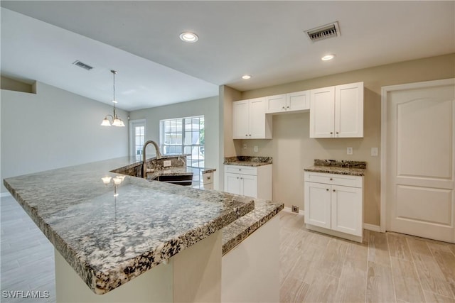 kitchen featuring stone counters, light wood-style flooring, a sink, white cabinetry, and a large island with sink